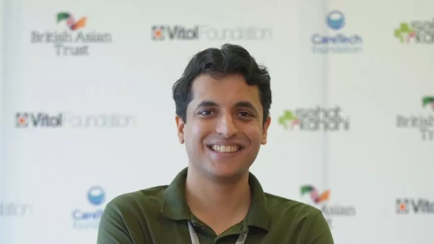 Ahsan has short dark wavy hair and is smiling at the camera. He's wearing a fern green polo shirt and has his arms folded across his chest.