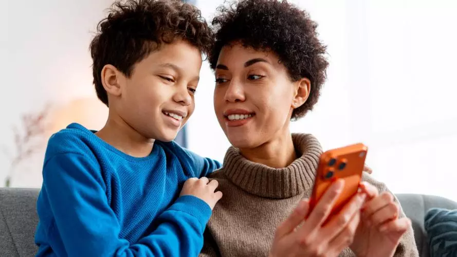 A mother and child sitting on a sofa, looking together at a phone