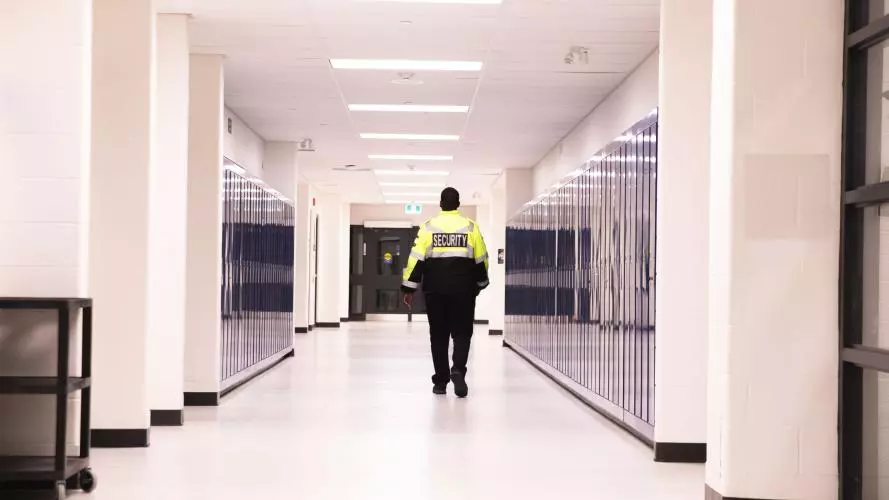 A security guard walks along a long school corridor lined by lockers