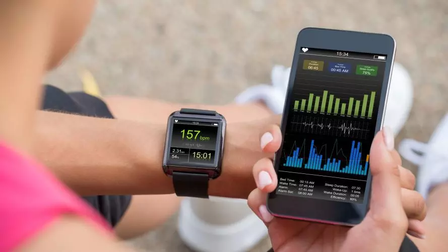 A runner wearing a smartwatch tracking their fitness statistics. They are holding their smartphone next to their wrist, looking at more detail on a fitness app.