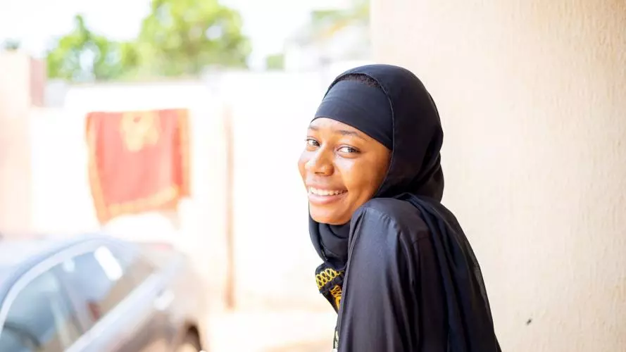 A young smiling Nigerian woman looking at the camera, holding a mobile phone