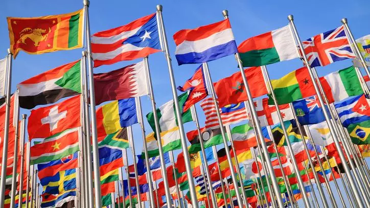 Multiple rows of national flags on flagpoles against a bright blue sky. 