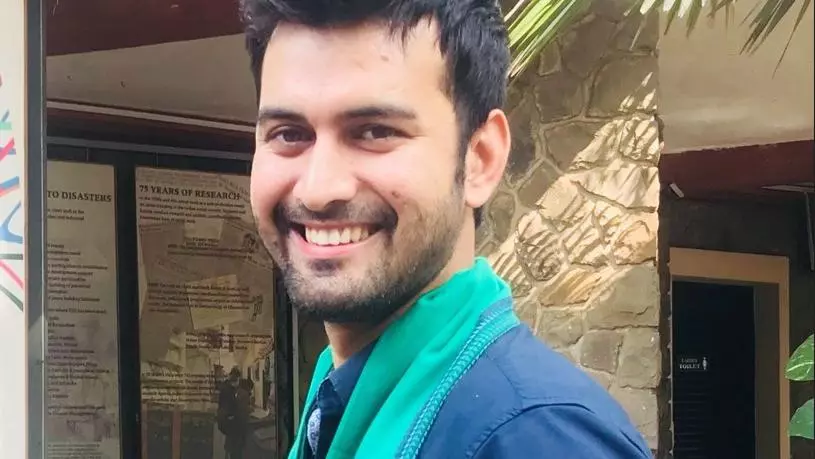 Sayyed Manzer has short black hair and a beard and is smiling at the camera.  