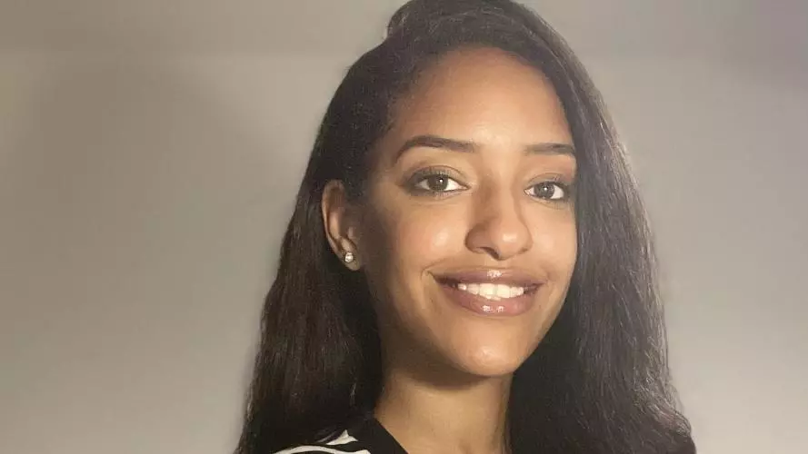 Bothaina has long black hair and is smiling at the camera. She's wearing a white top with a black and white horizontally-striped cardigan