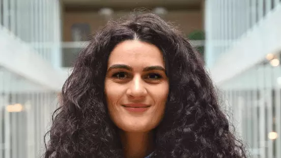 Charlene Calderaro wears a light blue shirt, has folded arms, and long dark curly hair. 