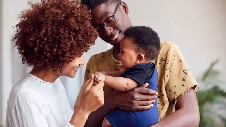 Two parents holding and playing with their young baby. 