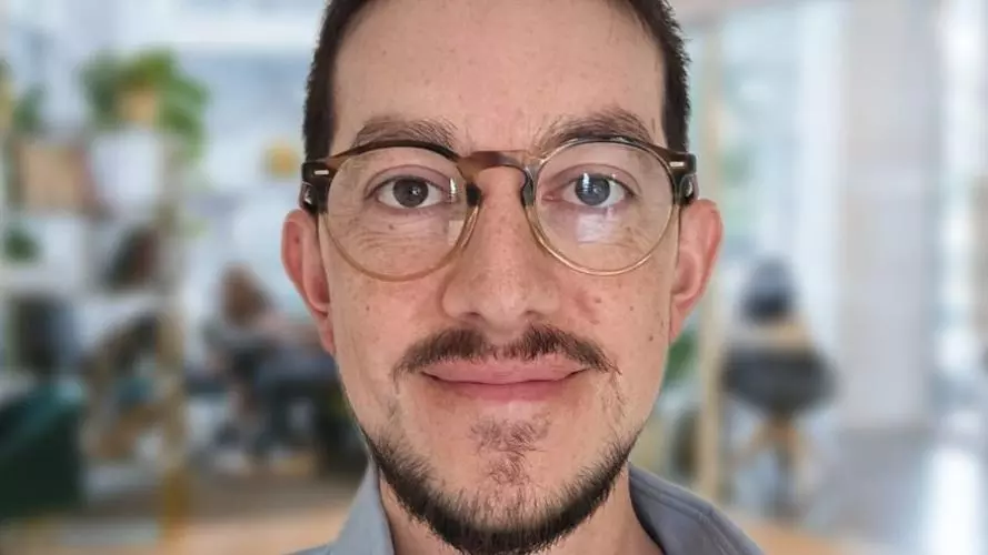 Hernando has short dark hair and a beard, and is wearing glasses. He is wearing a pale blue shirt.