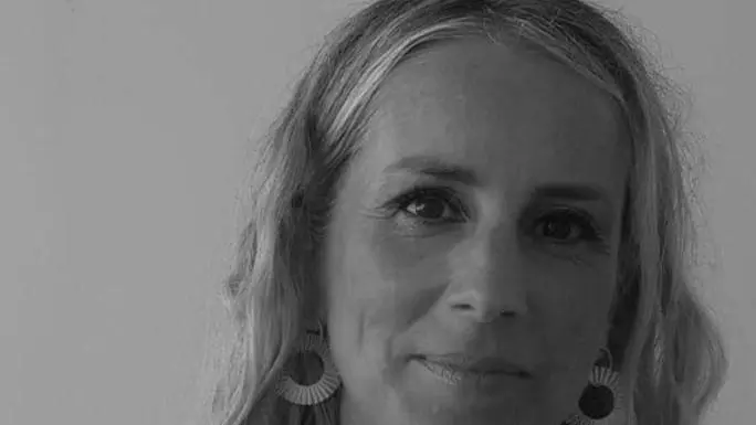 Lucy Olsen, has long shoulder length hair an smiling at the camera in a black and white photo.