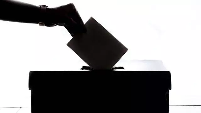A silhouette of a hand dropping a paper into a ballot box