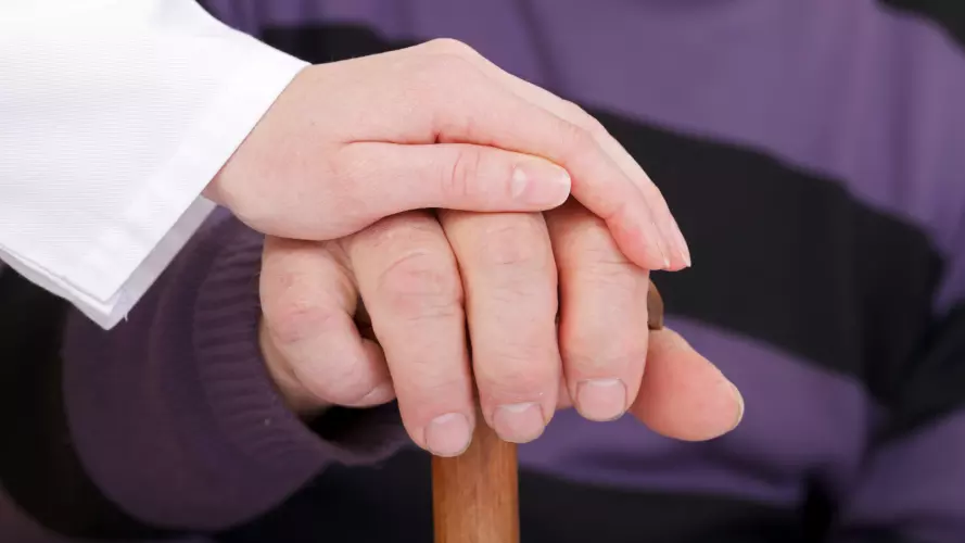 A young hand placed on top of an older hand resting on a walking stick.