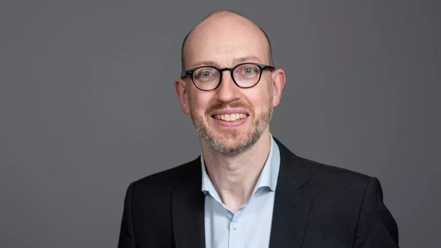 Arne Kuehl is wearing a suit and glasses smiling