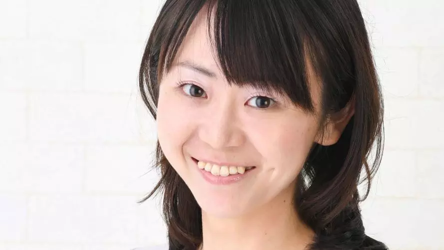 Aya has shoulder length black hair and a fringe. She's wearing a white top and pale grey jacket. 