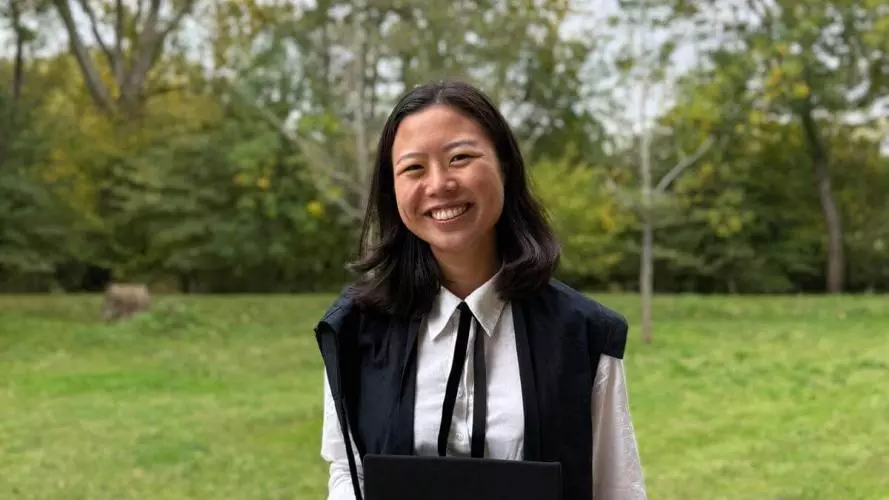 Christina Wang wears academic dress and is standing in front of a garden