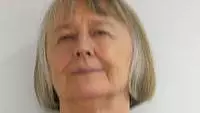 Mavis has short grey hair, she is wearing a necklace and a dark top.