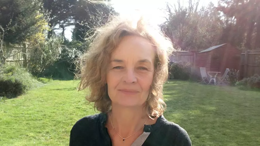 Elaine Chase has short blonde hair and is wearing a black top. She is standing in a grassy area.