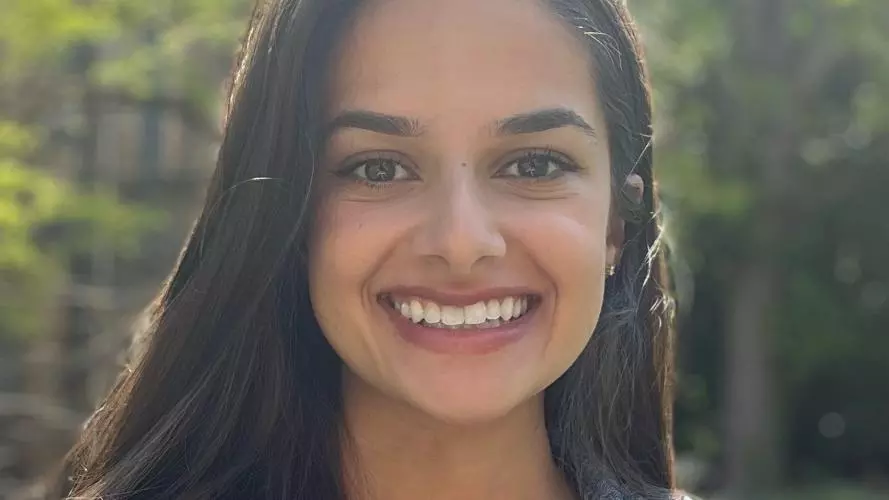 A headshot of Deanna Giraldi, with long dark shoulder-length hair, shows her smiling while wearing a denim jacket and looking directly at the camera.