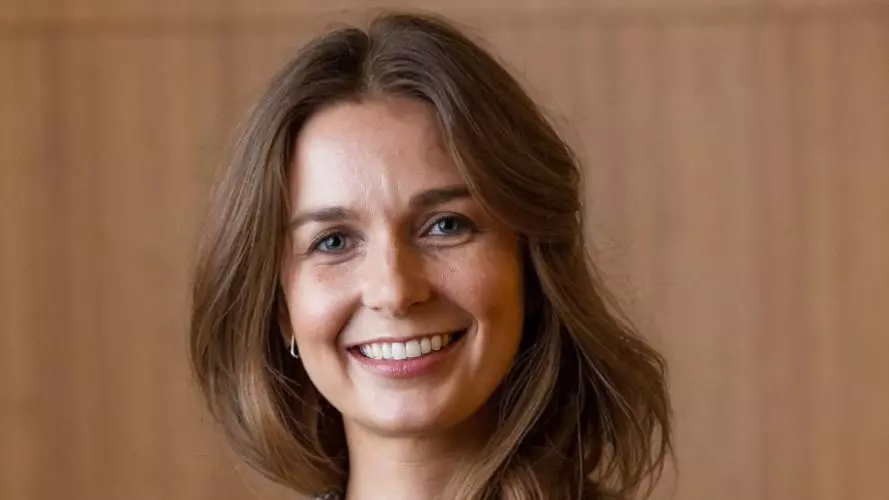 Cyrette Saunier wears a grey blazer and is smiling in front of a wood-panelled wall.
