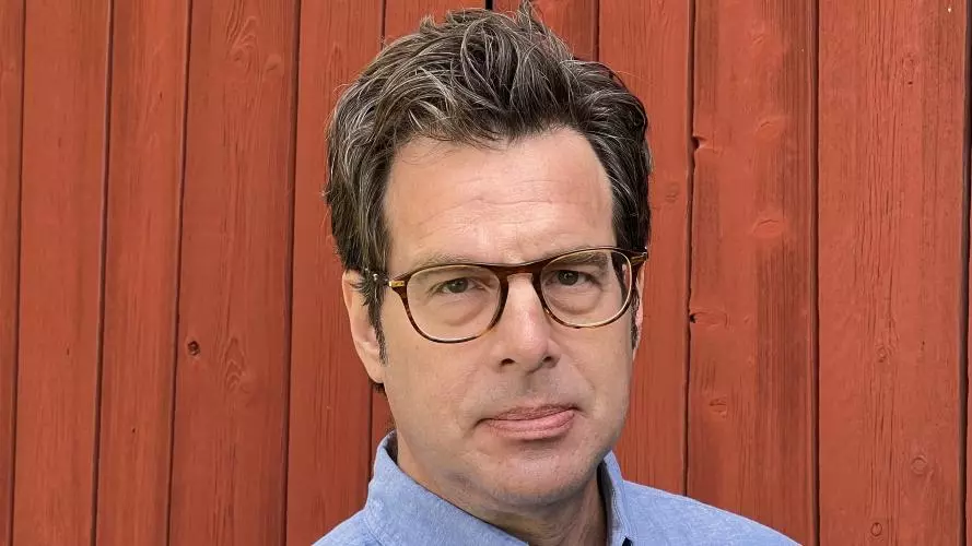 Kenneth Nelson is wearing glasses and a blue shirt looking directly at the camera.