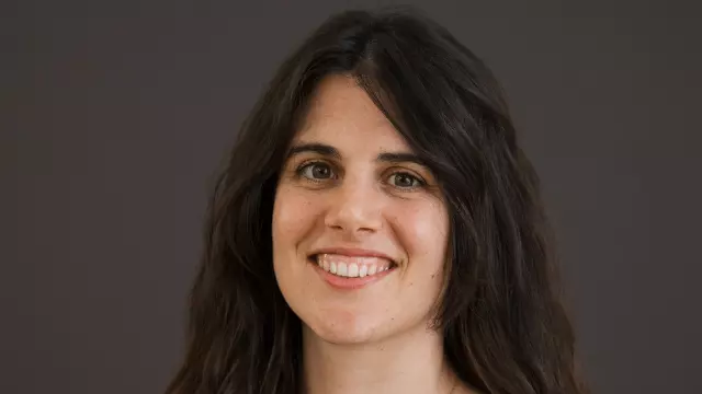 Woman with long brown hair, smiling at the camera and wearing a black dress with white pattern.