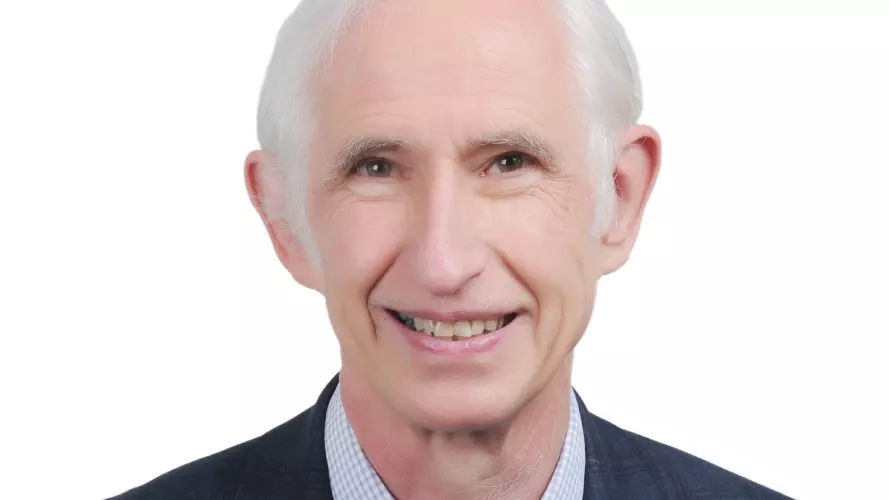 Robert  has grey hair and is smiling at the camera. He's wearing a shirt, tie and suit jacket 