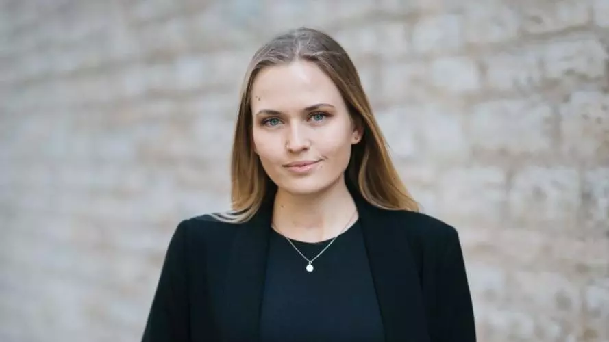 Moa Schafer has shoulder length blond hair, wearing a dark jacket looking at the camera. 