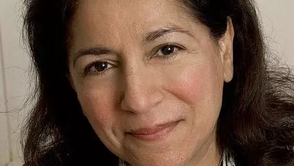 Rebecca Surender has long black hair and is wearing a brown jacket with white and brown scarf.
