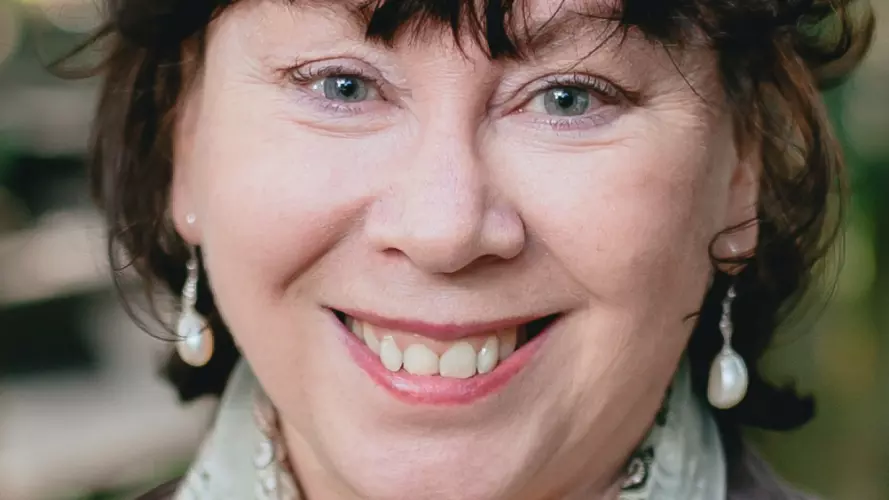 Woman with short brown hair, smiling broadly with a light green patterned scarf around her neck.