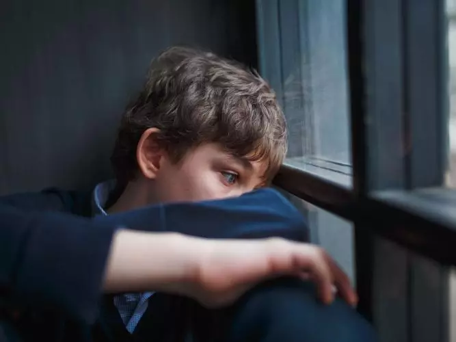 Boy sitting by a window with their head resting on folded arms, appearing contemplative
