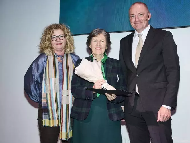 Three people are standing together at an award ceremony. Prof Daly is in the centre with short grey hair and wearing a dark checked jacket.