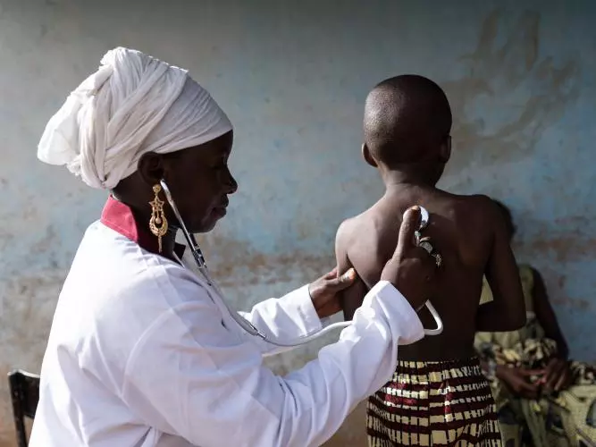 A nurse in a white uniform pressing a stethoscope to the back of a young child's back. Credit: Riccardo Niels Mayer - stock.adobe.com