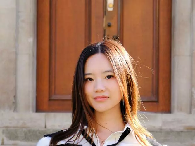 Vivian Gu wears academic dress, has long dark hair and stands in front of a set of steps