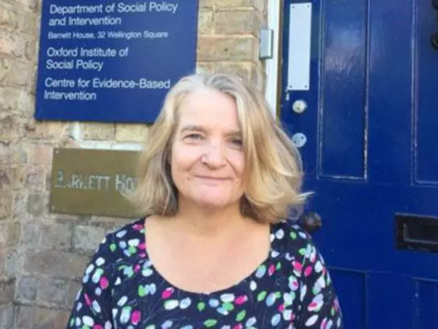 Smiling woman with light brown hair, wearing a patterned dress and standing in front of a dark blue door
