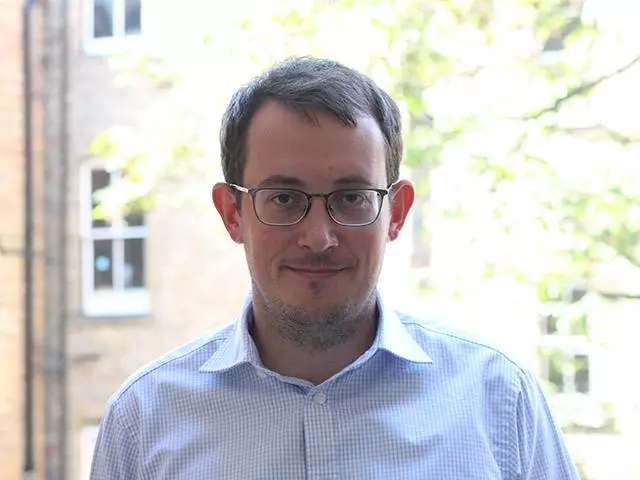 Man with short brown hair who is smiling and wearing dark rimmed glasses