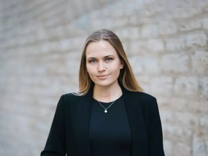 Moa Schafer has shoulder length blond hair, wearing a dark jacket looking at the camera. 