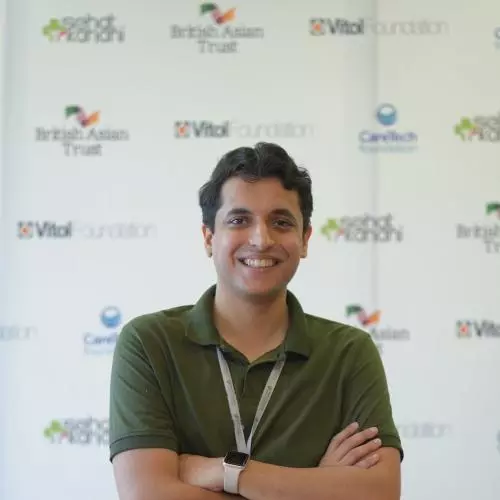 Ahsan has short dark wavy hair and is smiling at the camera. He's wearing a fern green polo shirt and has his arms folded across his chest.