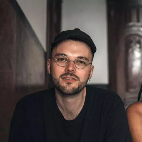 Steffen has short black hair, black beard and metal-rimmed glasses. He's wearing a black jumper 