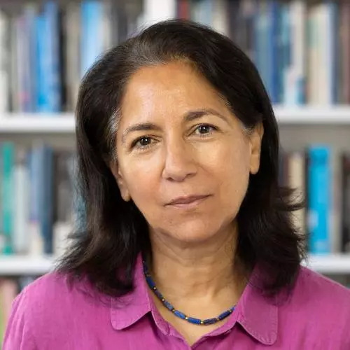 Rebecca Surender has shoulder-length dark hair. She is wearing a pink shirt, sitting in front of some bookshelves