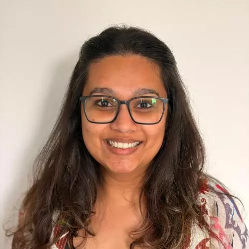 Shoumeli Das wears glasses and a blue top. She has long brown hair and is smiling.