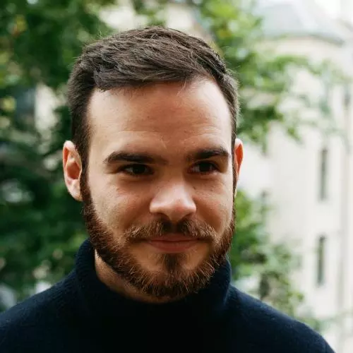 Man with dark brown hair and beard, wearing a black polo neck top