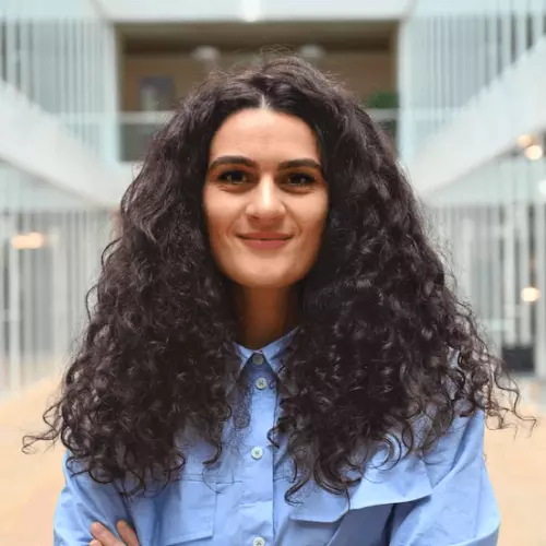 Charlene Calderaro wears a light blue shirt, has folded arms, and long dark curly hair. 