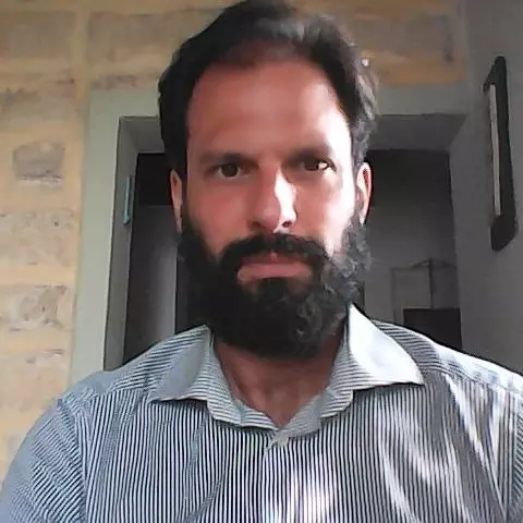 Paolo Graziano wears a blue striped shirt, has a beard, and is sitting in front of a brick wall