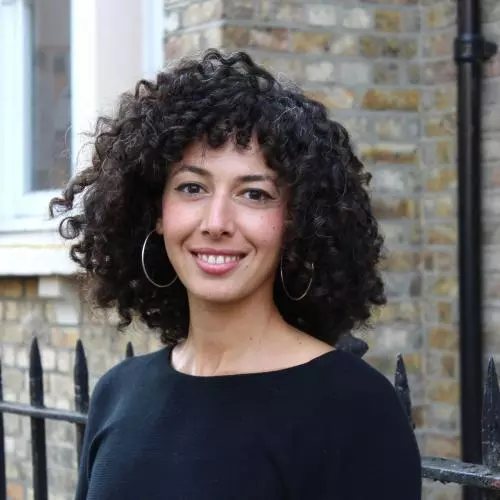 Rana Khazbak has curly black hair, wearing a black top with big silver hoop earrings smiling at the camera.