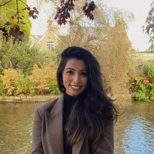 Saara has long dark hair, is wearing a brown suit jacket and is smiling at the camera. 