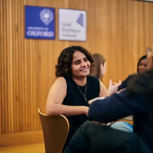 Shreyanka is sitting in a chair, wearing a black top and talking to someone off-camera.