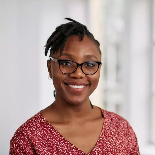 Sopuruchukwu has short black hair and is wearing glasses. She's wearing a red top with small white and pink patterns.  