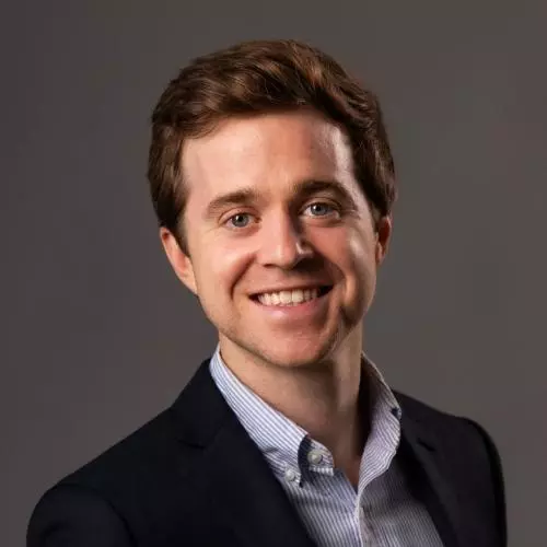 Zach Parolin has short brown hair. He is wearing a light blue shirt and a dark blazer, and smiling broadly. 