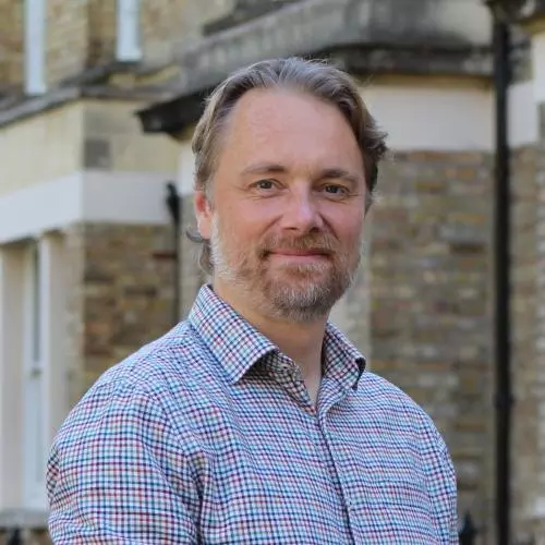 Mark Fransham is wearing a plaid shirt, with short blonde hair, a short bear and mostashe and smiling gentle at the camera.