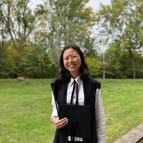Christina Wang wears academic dress and is standing in front of a garden