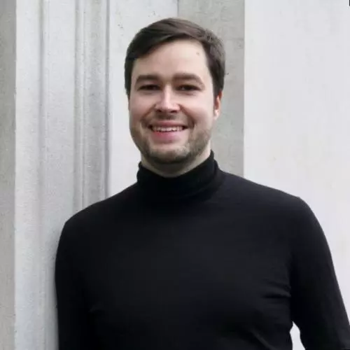 Christoph has short dark hair, a beard and is smiling at the camera. He's wearing a black polo neck top 