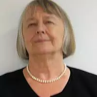 Mavis has short grey hair, she is wearing a necklace and a dark top.